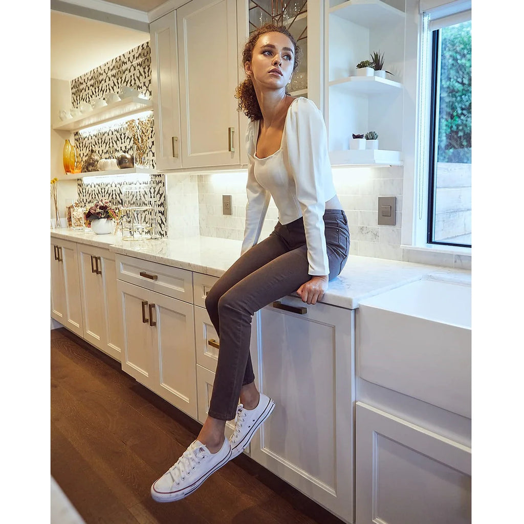 Woman on counter wearing brown stretchy high-rise skinny jeans and a white tee