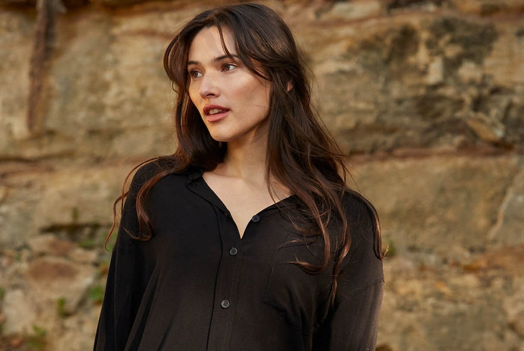 Women at the beach wearing jeans, a black button-up, and holding sunglasses