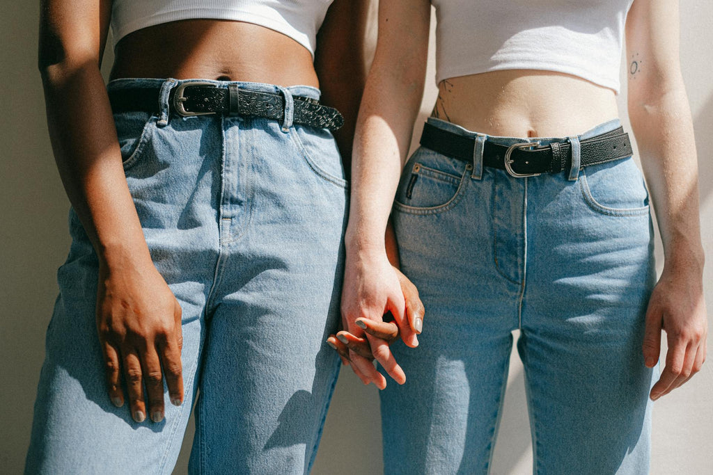 Two women in light wash jeans and white tees holding hands