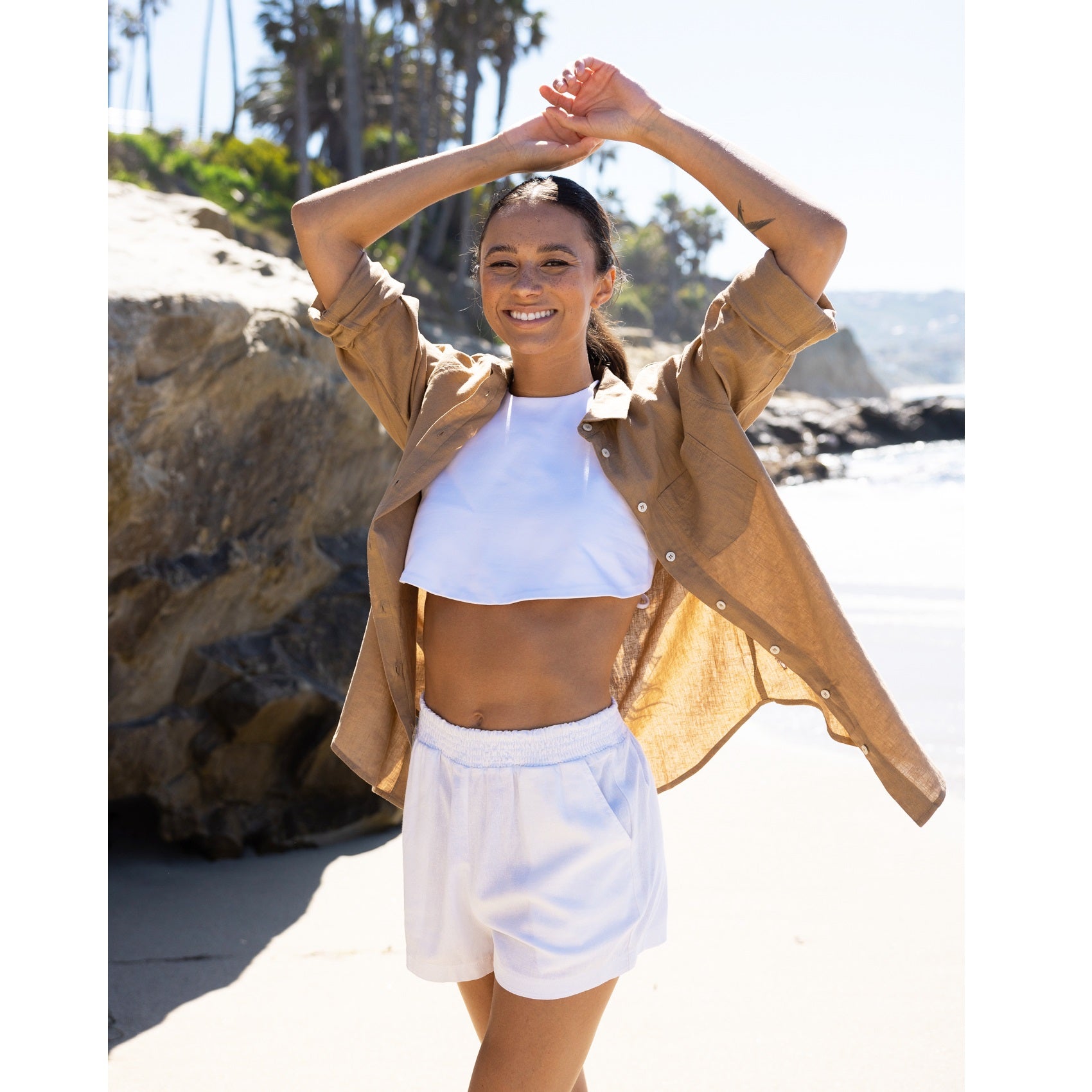 Woman wearing a brown linen shirt and white shorts and a cropped tee