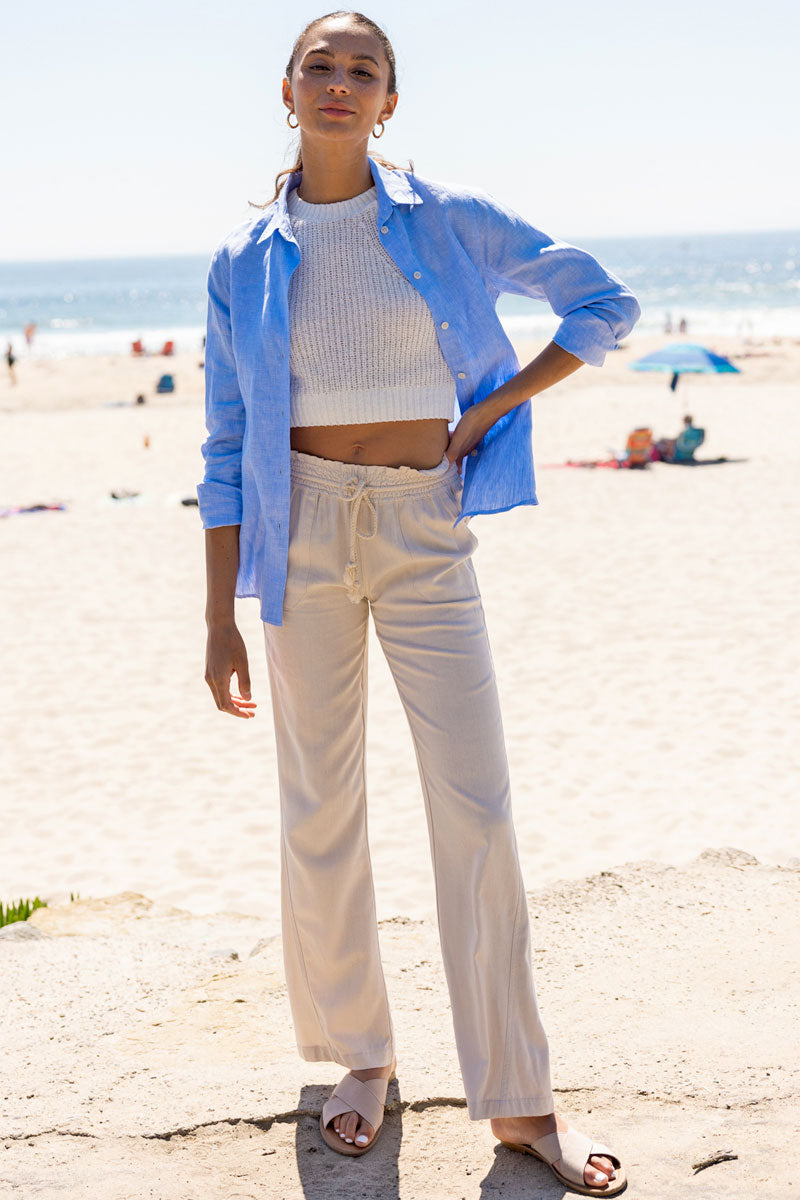 A woman at the beach wearing white linen pants and a blue linen shirt