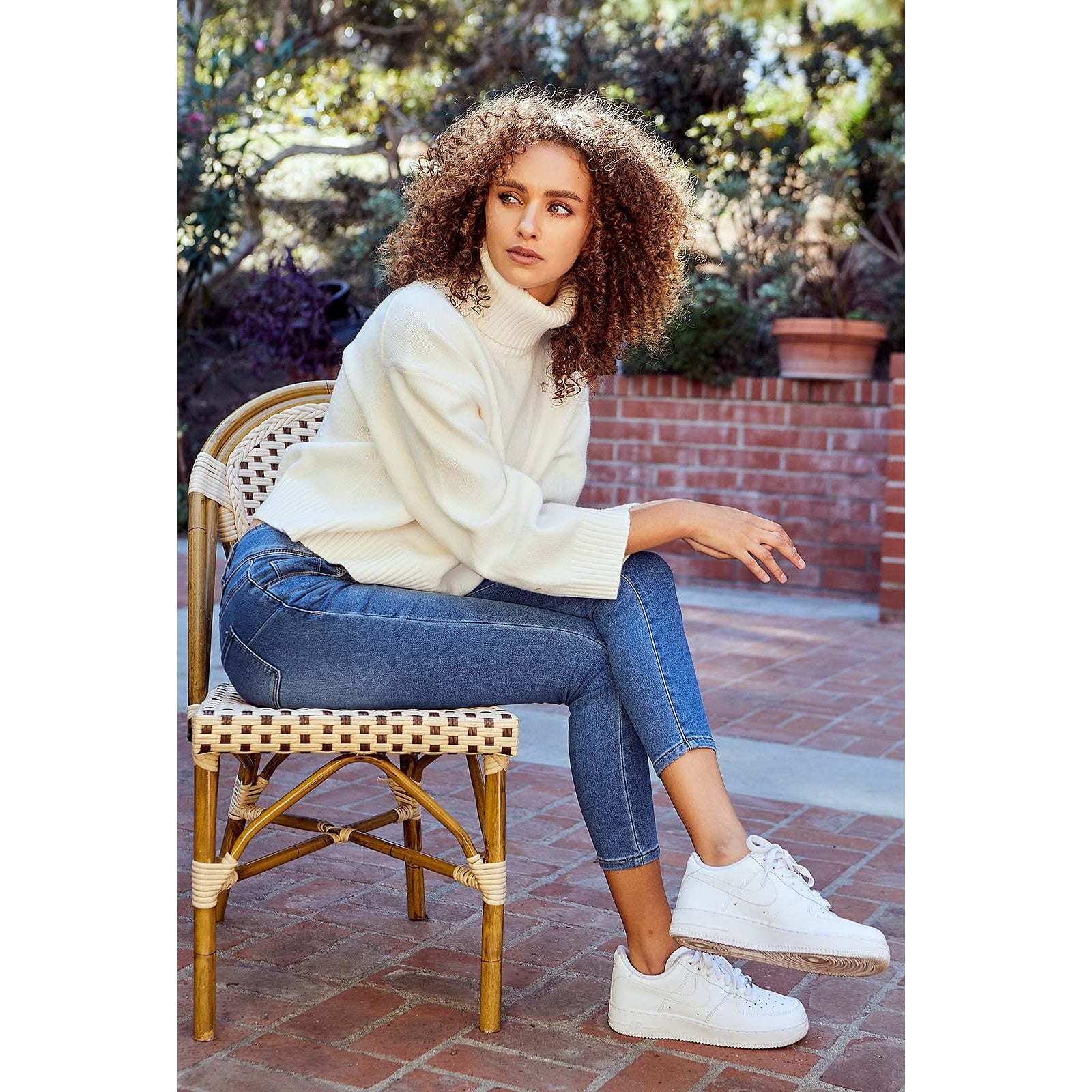 A woman sitting on a chair wearing a white pullover and skinny jeans