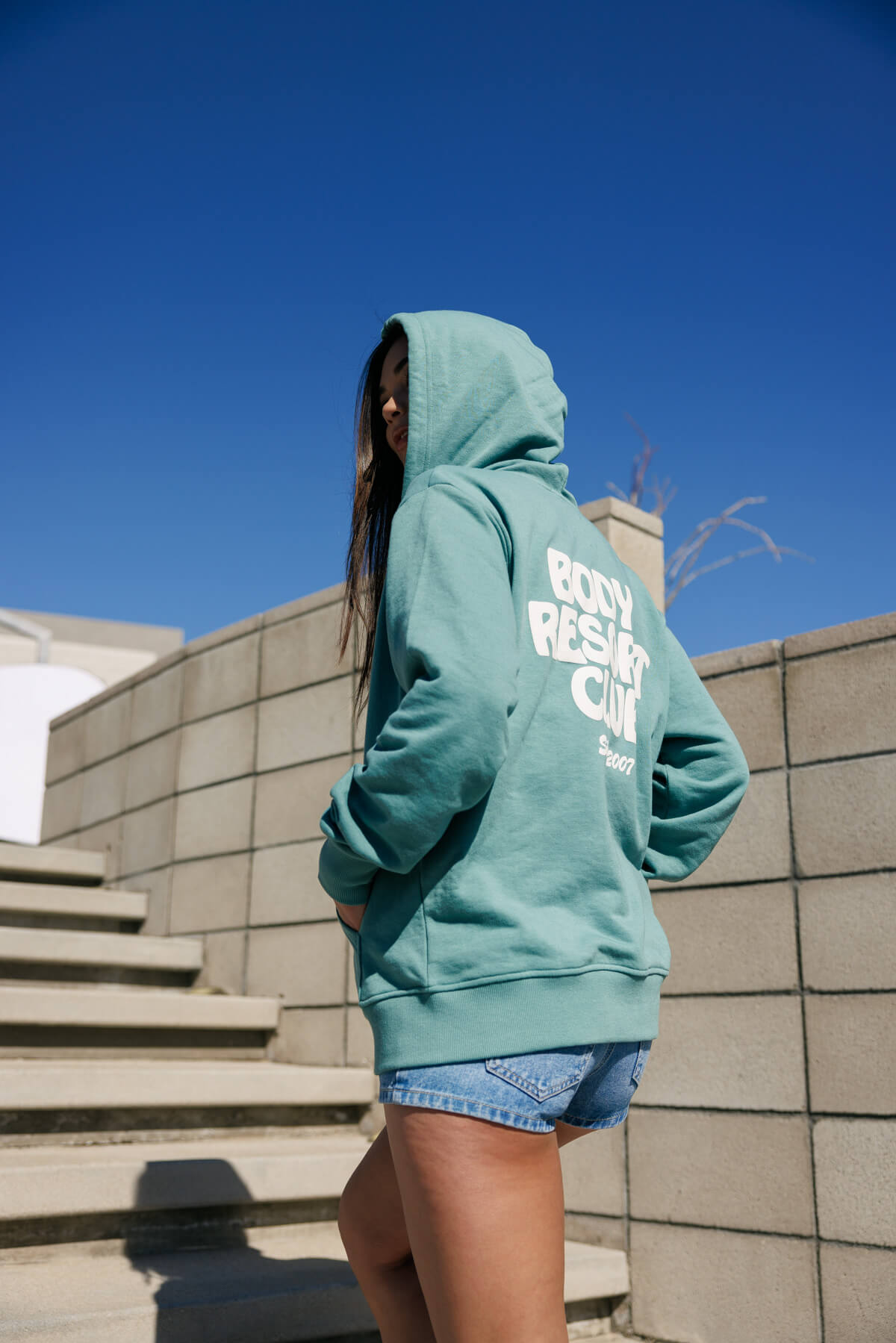 Woman on stairs wearing a green hoodie and denim shorts