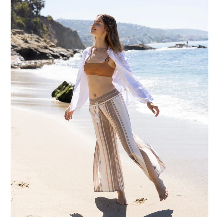A woman wearing wide linen pants with brown and white vertical stripes