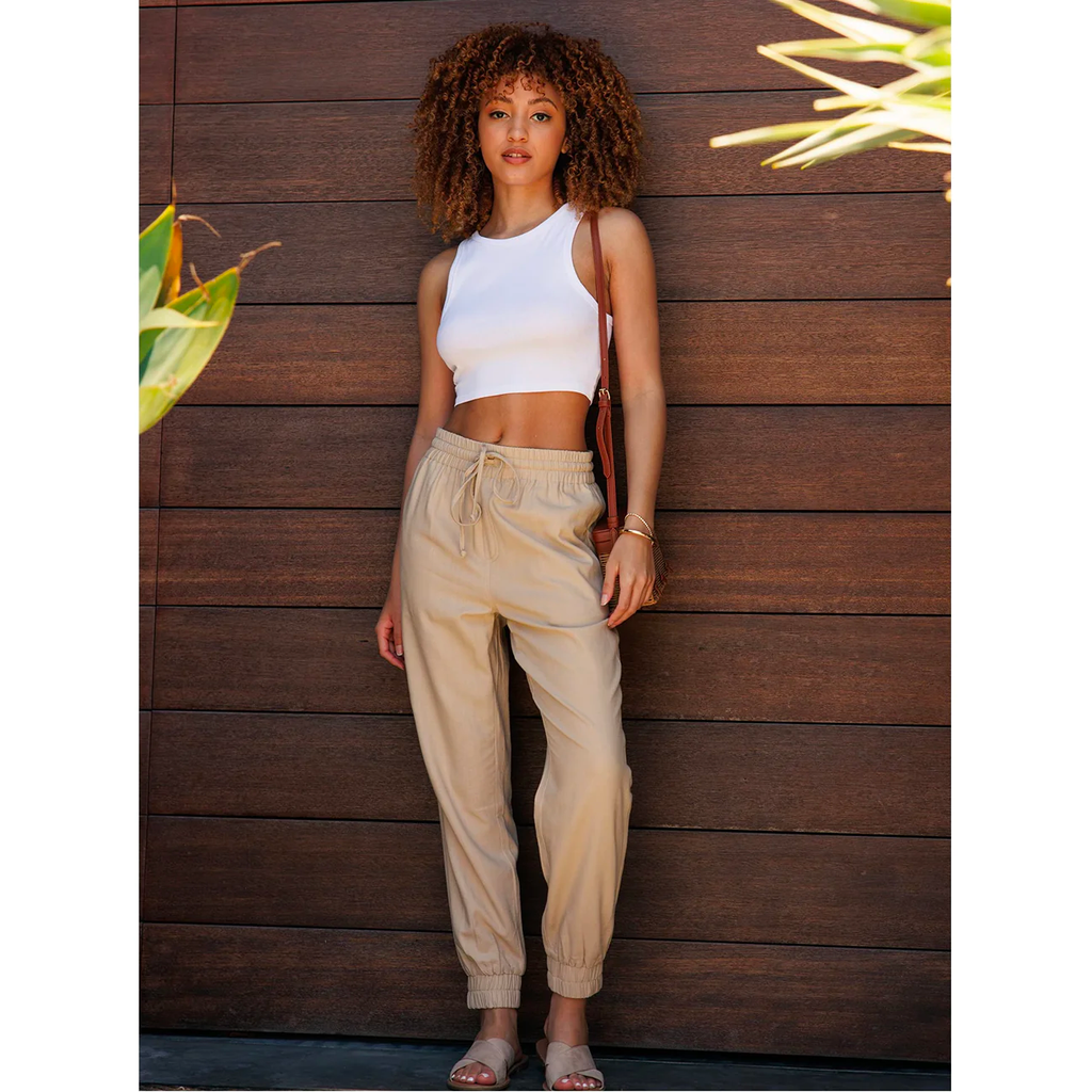 A woman in front of a wood wall wearing linen joggers