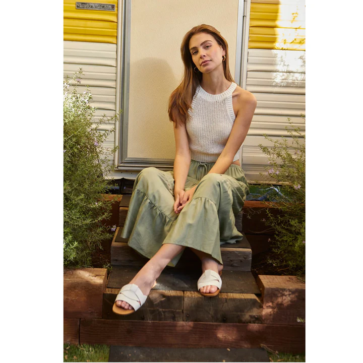 Woman sitting on stairs in a sage green beach linen skirt and a white tank top