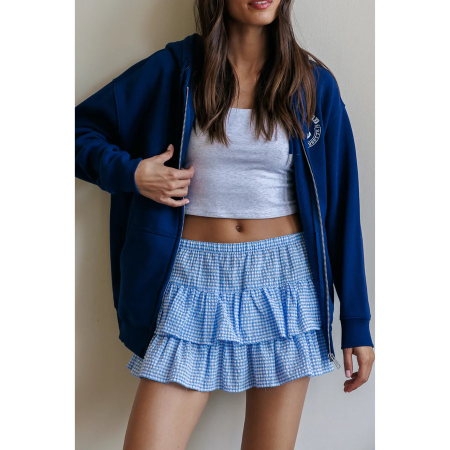 Woman in a white tee, navy zip-up hoodie, and blue tiered mini skirt