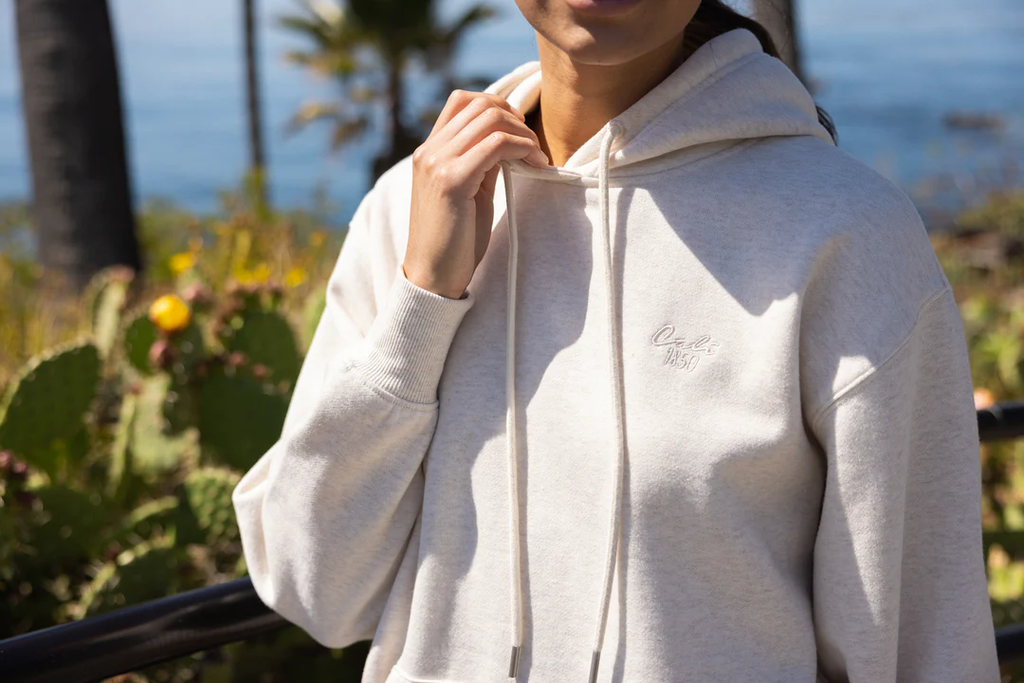 A woman wearing a cream oversized hoodie near the beach